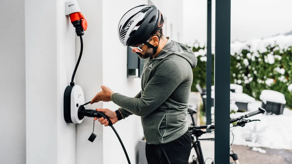 Mann mit Fahrradhelm steck Ladestecker für E-Bike in Steckdose